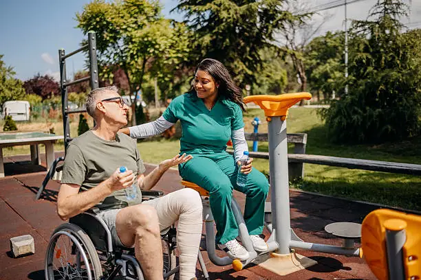 Homecare aide assisting wheelchair user at outdoor gym.