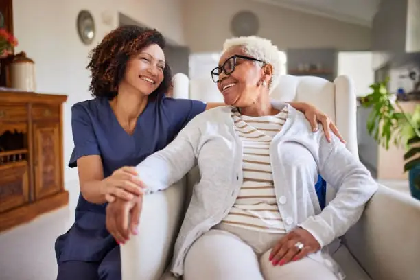 Caregiver and elderly woman smiling together at home.