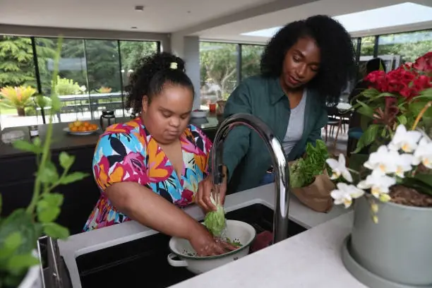 Two women washing lettuce in modern kitchen.